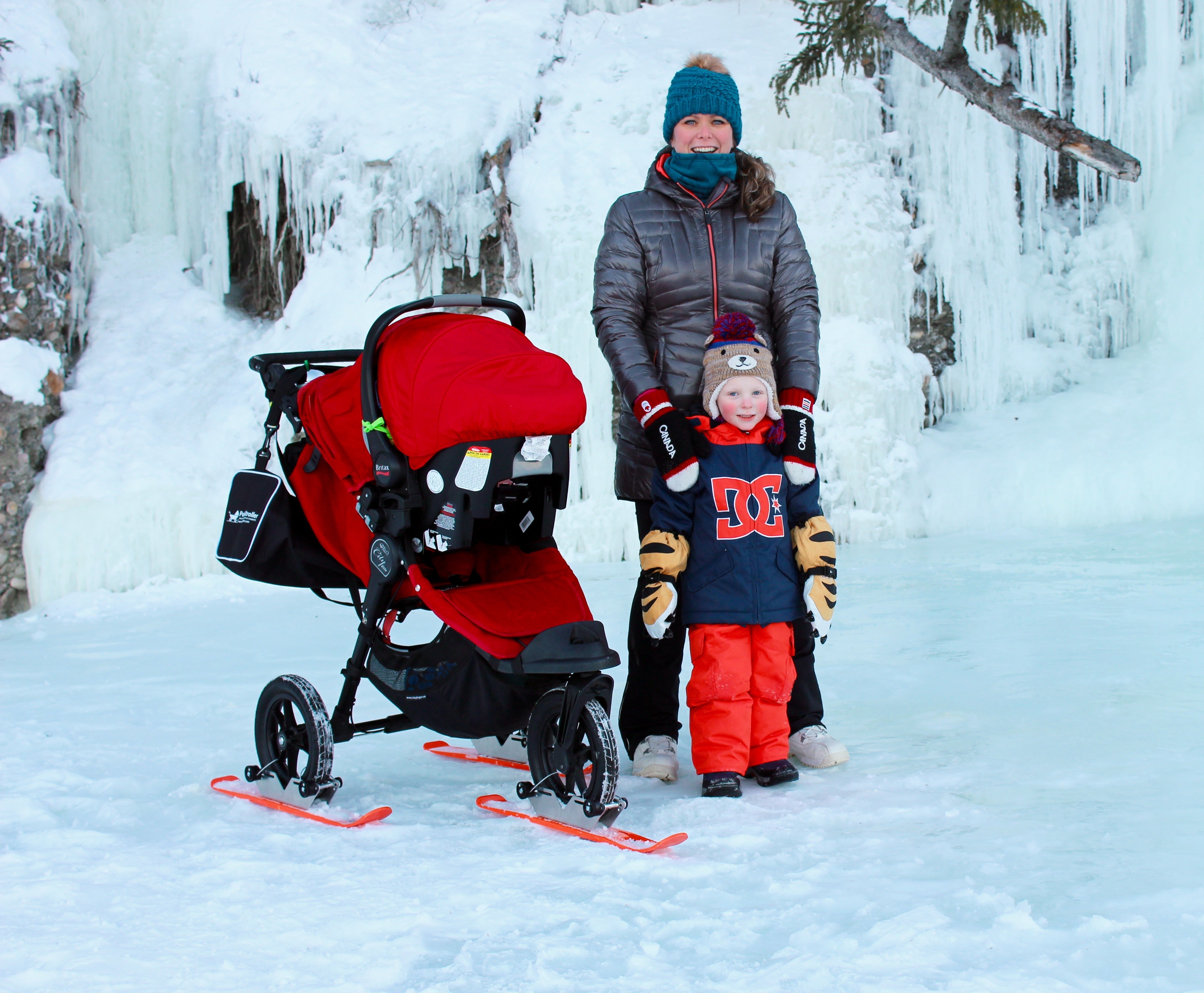 Person with a child in a snow-covered landscape with a red stroller.